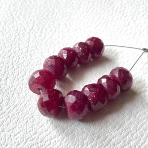 May include: A strand of deep red ruby beads, faceted and polished, strung on a silver wire. The beads are round and have a slightly irregular shape.
