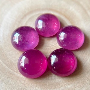 May include: Five round, pink cabochon gemstones. The gemstones are smooth and polished, with a high gloss finish.