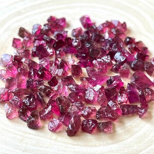 May include: A collection of pink and purple rough tourmaline gemstones. The gemstones are various sizes and shapes, and have a natural, unpolished finish.