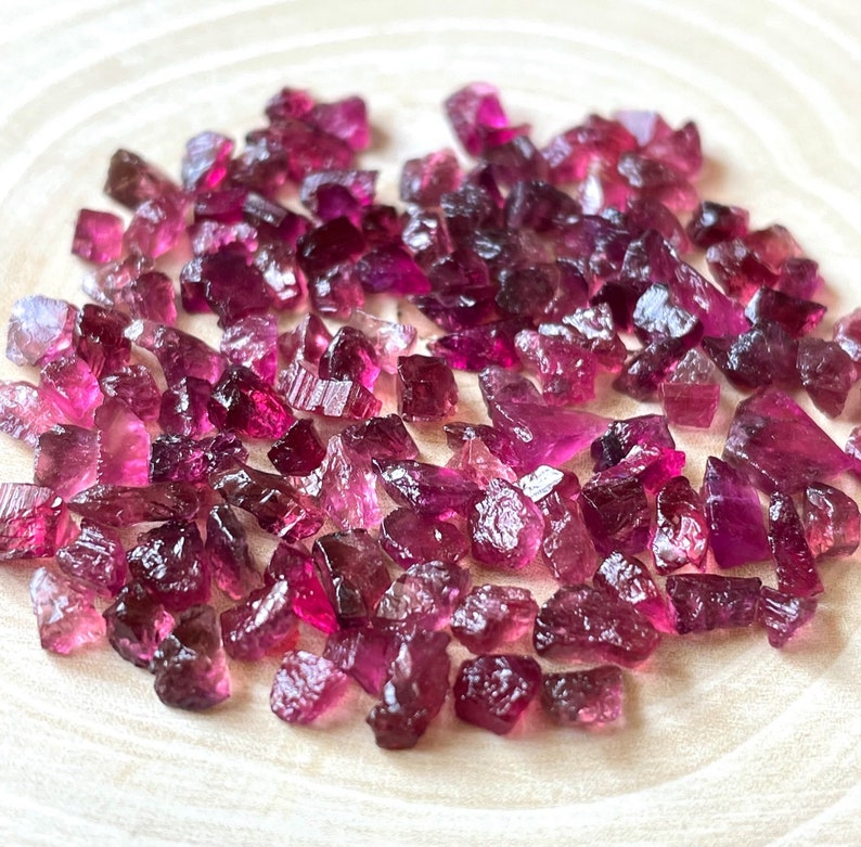 May include: A collection of pink and purple rough tourmaline gemstones. The gemstones are various sizes and shapes, and have a natural, unpolished finish.