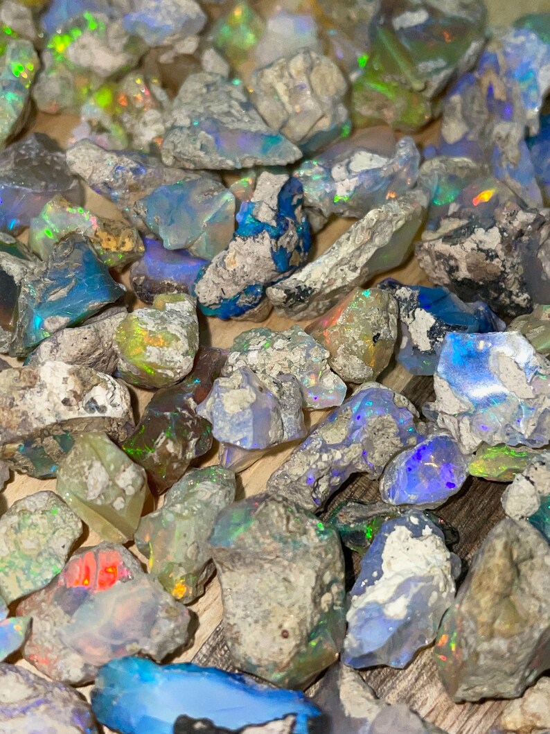 May include: A collection of rough opal stones in various shades of blue, green, and white. The stones are irregular in shape and have a natural, unpolished finish.