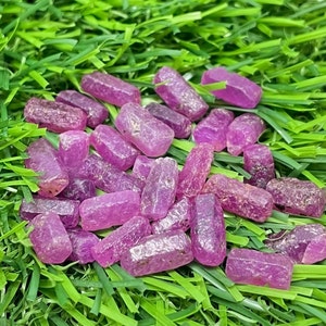 以下が含まれることがあります： 緑色の芝生の上に、長方形のピンク色のルビーの原石が並んでいます。