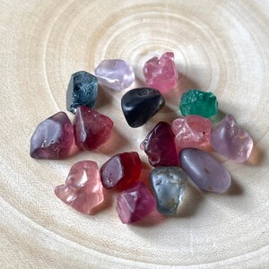 Puede incluir: Una colecci&oacute;n de 15 gemas de colores, incluyendo rosa, rojo, verde, azul y morado, mostradas sobre una superficie de madera clara.