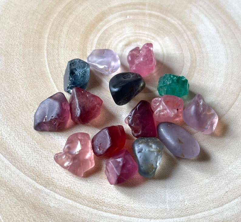 Puede incluir: Una colecci&oacute;n de 15 gemas de colores, incluyendo rosa, rojo, verde, azul y morado, mostradas sobre una superficie de madera clara.