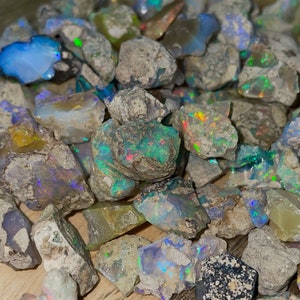 May include: A collection of rough, unpolished opal stones in various shades of gray, blue, green, and white. The stones have a natural, iridescent sheen.
