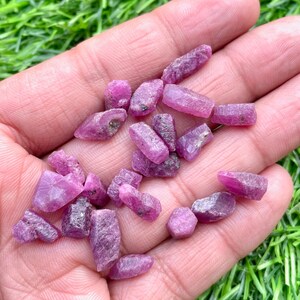 Pu&ograve; includere: Una collezione di piccoli cristalli di rubino rosa di varie forme e dimensioni. I cristalli sono grezzi e non lucidati, con una texture naturale e ruvida.
