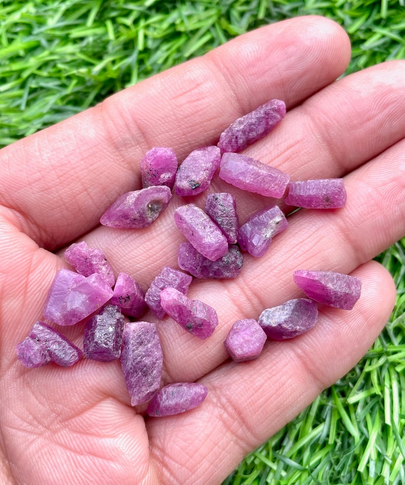 Pu&ograve; includere: Una collezione di piccoli cristalli di rubino rosa di varie forme e dimensioni. I cristalli sono grezzi e non lucidati, con una texture naturale e ruvida.
