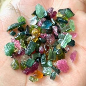 May include: A collection of small, colorful tourmaline crystals in various shades of green, pink, red, and yellow. The crystals are rough and have a natural, unpolished appearance.