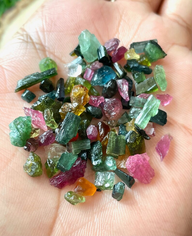 May include: A collection of small, colorful tourmaline crystals in various shades of green, pink, red, and yellow. The crystals are rough and have a natural, unpolished appearance.