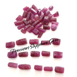 May include: A collection of raw, uncut ruby gemstones in varying sizes and shapes, displayed against a white background. The gemstones are a deep, rich red color, with a rough, natural texture. The text "Precious Sapphire Gem" is also visible.