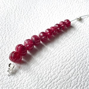May include: A strand of red ruby beads, each bead is carved with a floral design. The beads are strung on a silver wire.