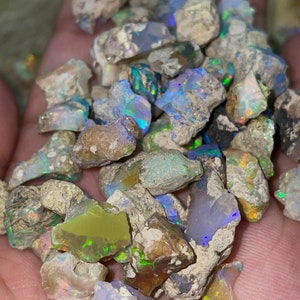 May include: A collection of rough opal stones in various shades of gray, white, green, and blue with iridescent flashes of color.