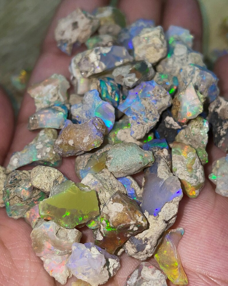 May include: A collection of rough opal stones in various shades of gray, white, green, and blue with iridescent flashes of color.