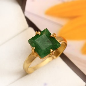 May include: A gold ring with a square emerald green gemstone.