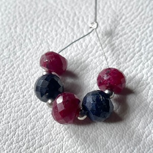 Puede incluir: Una hebra de cuentas de piedras preciosas con cuentas rojas y azules alternas. Las cuentas son facetadas y tienen un acabado pulido. Las cuentas están enhebradas en un alambre de plata.