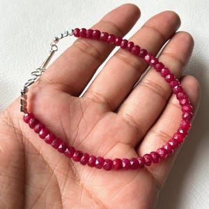 Puede incluir: Un brazalete de piedras preciosas rojas con un cierre de plata. El brazalete está hecho de pequeñas cuentas facetadas.