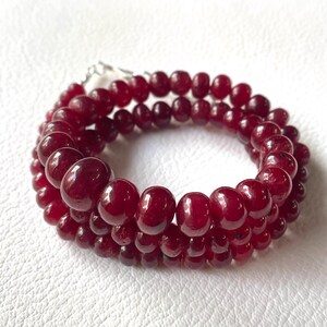 Puede incluir: Una hebra de cuentas de rubí rojo oscuro, enhebradas en un cordón plateado, con las cuentas dispuestas en forma circular.