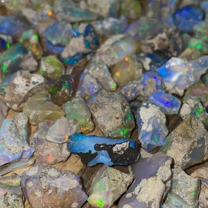 May include: A collection of rough, natural opal stones in various shades of blue, green, and white. The stones are scattered on a wooden surface.