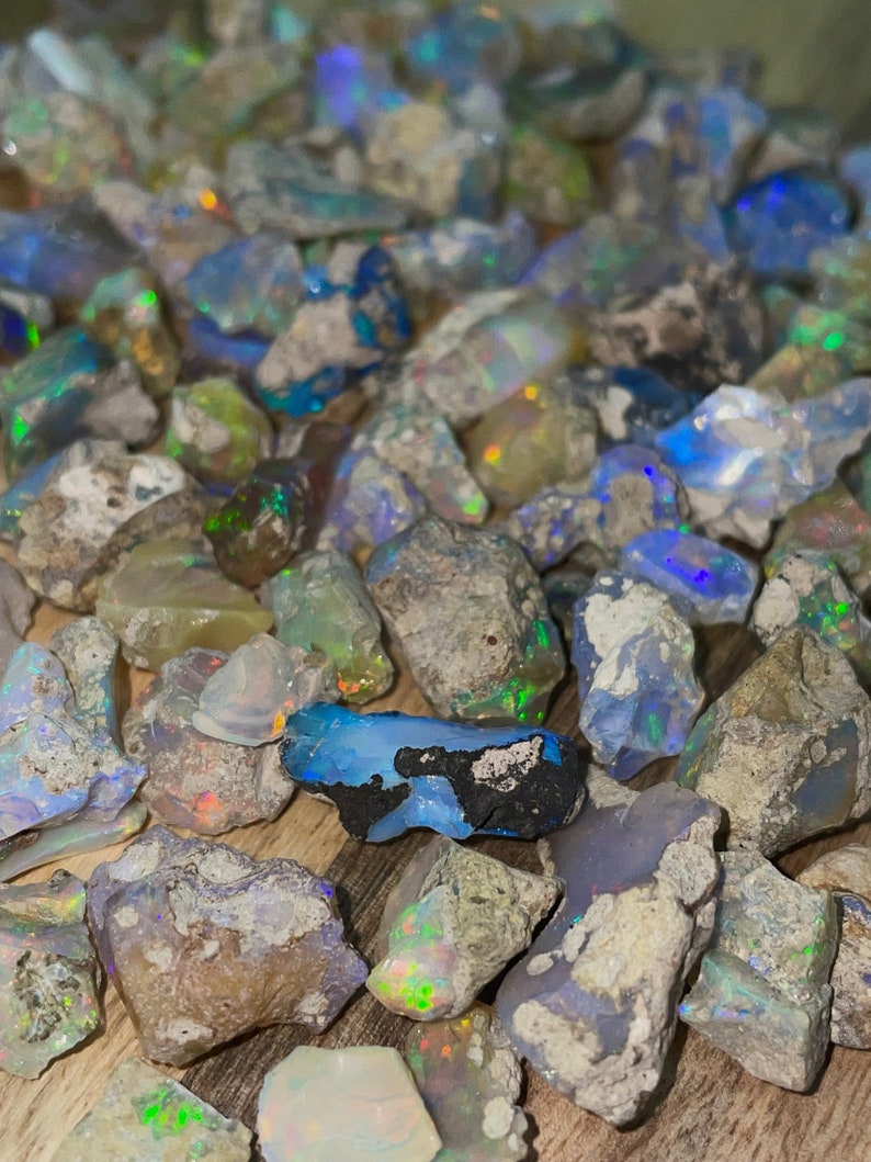May include: A collection of rough, natural opal stones in various shades of blue, green, and white. The stones are scattered on a wooden surface.