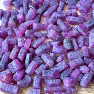 May include: A large pile of small, purple, rough-cut gemstones. The gemstones are all different shapes and sizes, but they are all a similar shade of purple.
