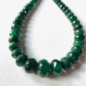 May include: A necklace composed of faceted, deep emerald green beads. The beads are strung together, creating a curved shape. The beads have a polished, reflective surface, and the necklace is displayed against a white background.