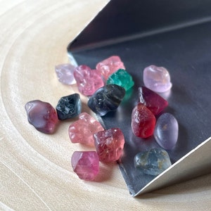 Puede incluir: Una colecci&oacute;n de piedras preciosas de colores, incluyendo rosa, rojo, verde y azul, se muestran en una pala de plata. Las piedras preciosas son de varias formas y tama&ntilde;os.