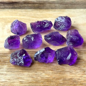 Puede incluir: Una colección de diez cristales de amatista en bruto de diferentes tamaños y formas. Los cristales son de color morado intenso y tienen un acabado natural sin pulir.