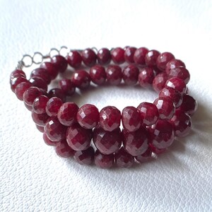 May include: A red gemstone bracelet with faceted beads. The bracelet is made of three strands of beads and has a silver clasp.