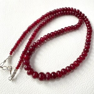 Puede incluir: Un collar hecho de cuentas de rubí rojo oscuro. El collar está enhebrado en una cadena de plata con un cierre.