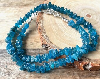 Puede incluir: Un collar de doble cadena hecho con chips de piedras preciosas azul turquesa. El collar está enhebrado en alambre plateado con un cierre plateado.