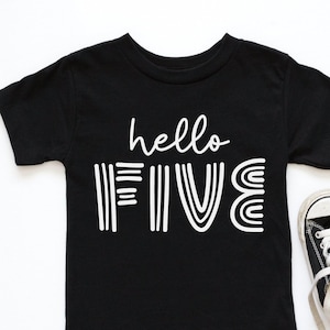 Puede incluir: Camiseta negra con texto blanco que dice "hello five" en una fuente divertida. La camiseta está sobre un fondo blanco con un par de zapatillas negras.