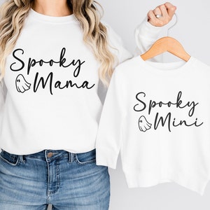 May include: White long-sleeved shirts with a ghost graphic and the text "Spooky Mama" and "Spooky Mini" printed on them.