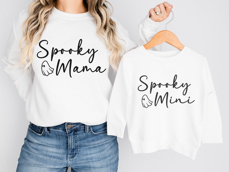 May include: White long-sleeved shirts with a ghost graphic and the text "Spooky Mama" and "Spooky Mini" printed on them.