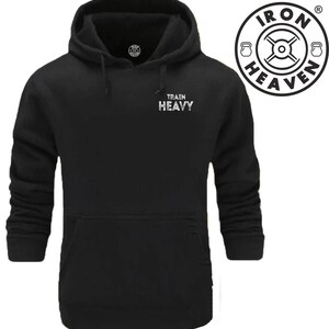 Op de afbeelding: Zwart hoodie met een witte print op de zak die "Train Heavy" zegt. De hoodie heeft een kangoeroezak en een capuchon met trekkoord.