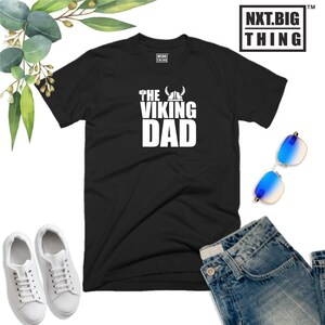 May include: Black t-shirt with white text that reads "The Viking Dad" and a graphic of a Viking helmet and axe.