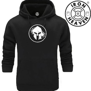 Peut inclure: Sweat-shirt à capuche noir avec un graphique blanc d'un casque de spartiate à l'intérieur d'un cercle avec un effet de projection. Le texte "IRON HEAVEN" est dans un cercle avec un poids de chaque côté.