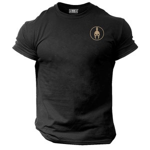 Könnte beinhalten: Schwarzes T-Shirt mit Rundhalsausschnitt und einem kleinen, kreisförmigen Emblem mit einem goldenen Spartanerhelm. Das Shirt hat kurze Ärmel und eine klassische Passform. Der Markenname ist oben in Weiß aufgedruckt.