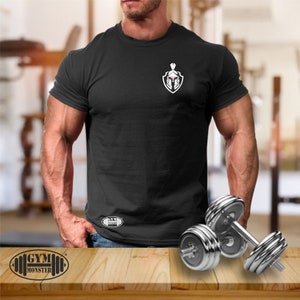 Könnte beinhalten: Schwarzes T-Shirt mit einer weißen Grafik eines spartanischen Kriegerhelms auf einem Schild. Das Shirt hat den Text "GYM" unten links aufgedruckt.