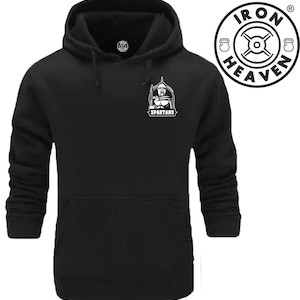 Op de afbeelding: Zwarte hoodie met een witte afbeelding van een Spartaanse krijger die een speer vasthoudt en het woord "SPARTANS" eronder. De hoodie heeft een kangoeroezak en een capuchon met trekkoord. Het Iron Heaven-logo bevindt zich in de rechterbovenhoek.