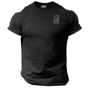 May include: Black crew neck t-shirt featuring a small, faded American flag design on the upper left chest. The shirt has short sleeves and a tag at the back of the neck. The fabric appears to be a soft, textured material.