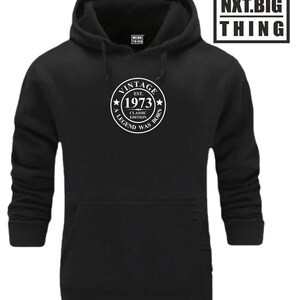 Op de afbeelding: Zwart hoodie met een witte cirkelvormige afbeelding met de tekst "Vintage Est. 1973 Classic Edition A Legend Was Born".