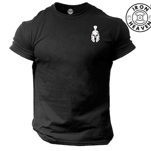 Puede incluir: Camiseta negra con un gráfico de casco espartano blanco en el pecho izquierdo. La camiseta tiene cuello redondo y mangas cortas. El texto "IRON HEAVEN" está impreso en blanco sobre un círculo negro con un logotipo de levantamiento de pesas.