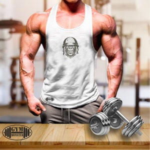 Può includere: Canotta bianca senza maniche con una grafica di un gorilla che indossa un casco. Il testo "GYM MONSTER" è sul fondo della canotta.