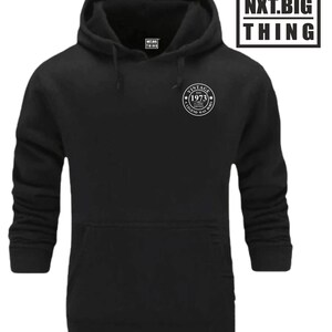 Op de afbeelding: Zwart hoodie met een witte print op de zak die "Vintage Est. 1973 A Classic Edition A Legend Was Born" zegt. De print is in een cirkel met een ster aan elke kant.