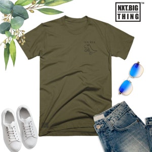 May include: A green t-shirt with a graphic of a dinosaur holding a cup of tea. The text "TEA-REX" is above the dinosaur. The t-shirt is laid flat on a white background with a pair of blue sunglasses, a pair of white sneakers, and a pair of blue jeans.
