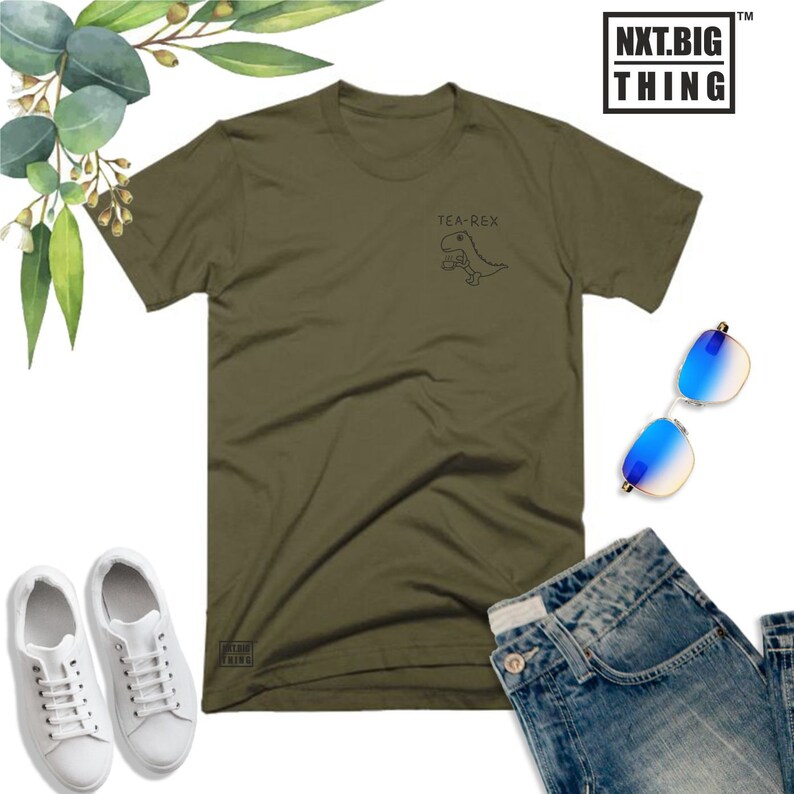 May include: A green t-shirt with a graphic of a dinosaur holding a cup of tea. The text "TEA-REX" is above the dinosaur. The t-shirt is laid flat on a white background with a pair of blue sunglasses, a pair of white sneakers, and a pair of blue jeans.