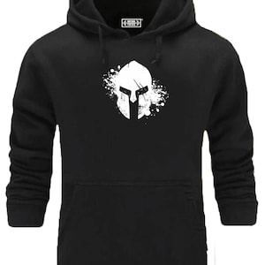 Peut inclure: Sweat-shirt à capuche noir avec un graphique blanc d'un casque de spartiate avec un effet de projection blanche derrière. Le texte "Fitness Thing" est sur une étiquette blanche sur le devant du sweat-shirt.