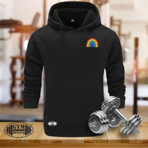 Könnte beinhalten: Schwarzer Kapuzenpullover mit einem Regenbogen-Motiv auf der linken Brust. Der Pullover hat eine Kängurutasche und eine Kapuze mit Kordelzug.