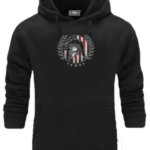 Könnte beinhalten: Schwarzer Kapuzenpullover mit einem Grafikdruck eines Spartanerhelms vor einer amerikanischen Flagge mit einem Lorbeerkranz darum. Der Text "Fitness Thing" befindet sich in einem kleinen Kästchen über dem Grafikdruck.