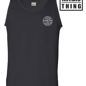 Op de afbeelding: Zwart tanktop met een witte cirkelvormige afbeelding met de tekst "Vintage Est. 1973 Classic Edition A Legend Was Born" en de tekst "NXT.BIG THING" in een zwart rechthoek.